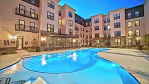 A modern hotel with a central swimming pool, multiple balconies, and a well-lit exterior.