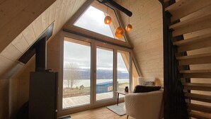 A cozy attic room with a large skylight, a fireplace, and a view of a lake. - Hengifosslodge Tiny Houses (Egilsstadír)