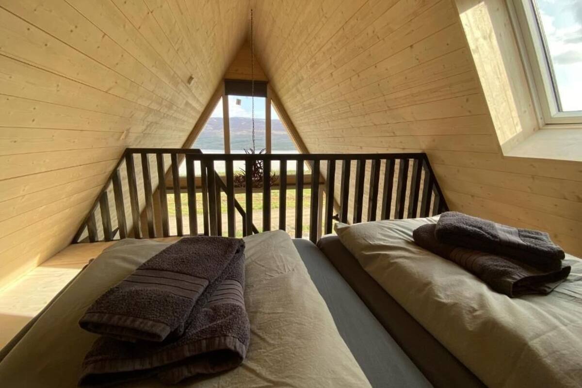 Une chambre confortable située sous les toits, avec deux lits, des poutres en bois et une vue sur l’extérieur.