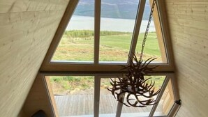 A cozy interior with a large window, a hanging light fixture, and a sofa. - Hengifosslodge Tiny Houses (Egilsstadír)