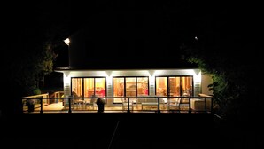 Une maison moderne dotée de grandes portes et fenêtres en verre, d’un patio couvert et d’un intérieur bien éclairé.