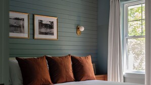 Une chambre à coucher avec un grand lit, un plancher en bois, une fenêtre avec des rideaux et deux tableaux encadrés accrochés au mur.