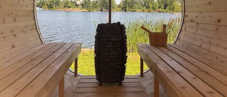 A wooden cabin with a circular window leading to a lake view. Inside, there are two wooden benches and a stone pillar.