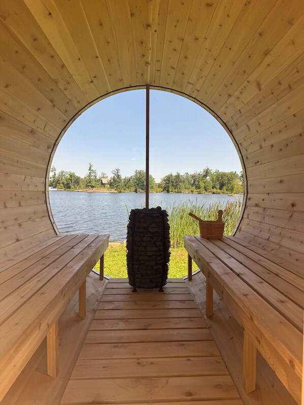 A wooden cabin with a circular window leading to a lake view. Inside, there are two wooden benches and a stone pillar.