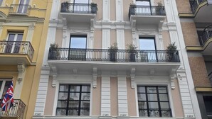 Un edificio de varios pisos con una entrada central, balcones con barandillas negras y un escaparate con un cartel.