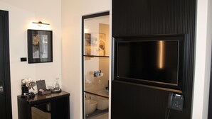 Un baño moderno con inodoro, bidé y mampara de vidrio. Hay una mesita con una cafetera y un teléfono.