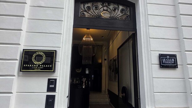 La entrada al Palacio Sparano, con un vestíbulo a rayas blanco y negro, un candelabro y un cartel con el nombre del hotel.