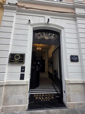 The entrance to the Sparano Palace, featuring a black and white striped entrance, a chandelier, and a sign indicating the hotel's name.
