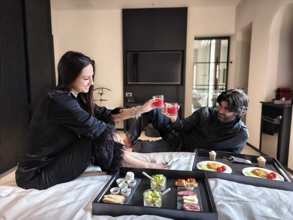 A modern hotel room with a bed, a tray of snacks, and a TV in the background.