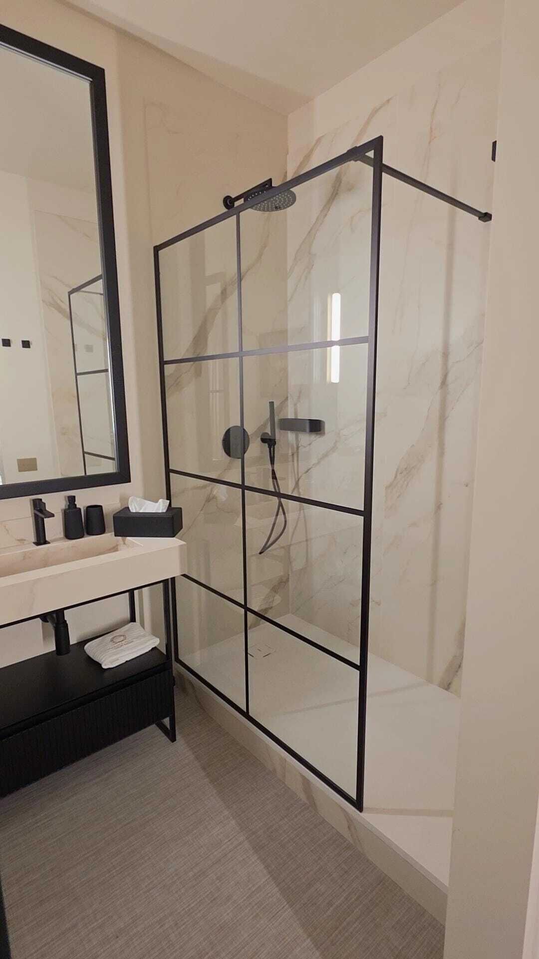 Une salle de bain moderne avec une douche à parois de verre, un grand miroir et un meuble-lavabo noir sur lequel est posée une serviette.