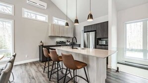 A modern kitchen with a central island, bar stools, and pendant lighting.