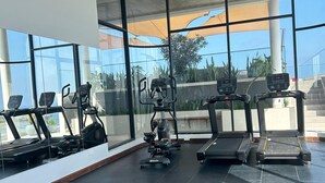 Una palestra moderna con tapis roulant, macchinari ellittici e una panca. Ampie finestre offrono vista sull'esterno.
