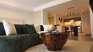 Un soggiorno moderno con un divano verde, un tavolino in legno e una cucina sullo sfondo.