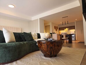Ein modernes Wohnzimmer mit einem grünen Sofa, einem Holztisch und einer Küche im Hintergrund.