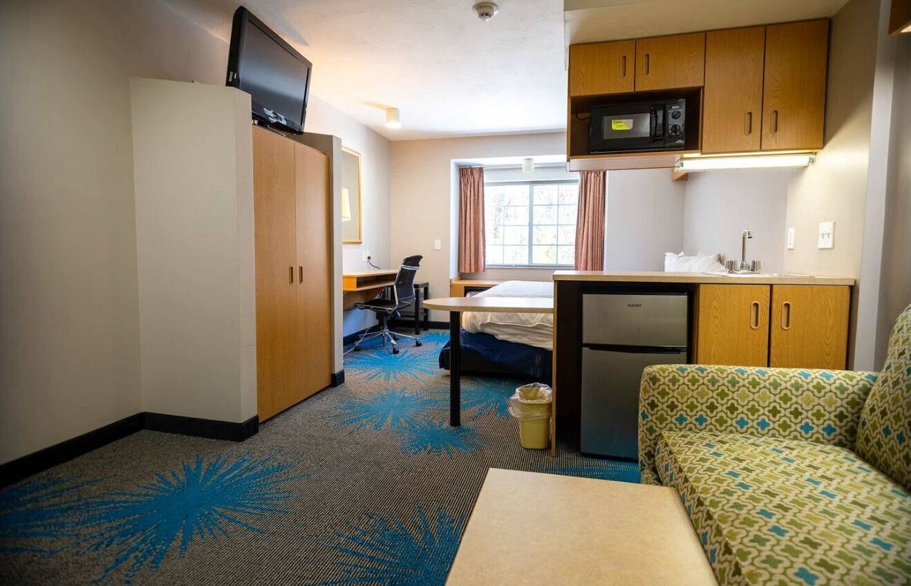 A compact hotel room with a kitchenette, a bed, a desk, and a sofa.