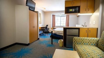 A compact hotel room with a kitchenette, a bed, a desk, and a sofa.