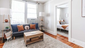 Un salon moderne avec un canapé, une table basse et un lampadaire. Il y a une fenêtre avec des rideaux et une porte qui donne sur une autre pièce.
