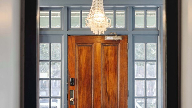 Une porte en bois avec un panneau de verre, un lustre et une fenêtre à cadre bleu.