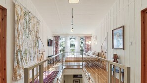 Un passadís espaiós amb terra de fusta, barana metàl·lica i vista d'una habitació amb llit i finestra.