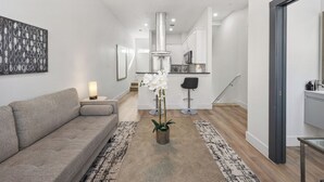 A modern living room with a grey sofa, a coffee table, and a potted orchid. A staircase leads to the kitchen area. - Perfect 1-bedroom townhome with rooftop in charming Fort Worth (Fort Worth)
