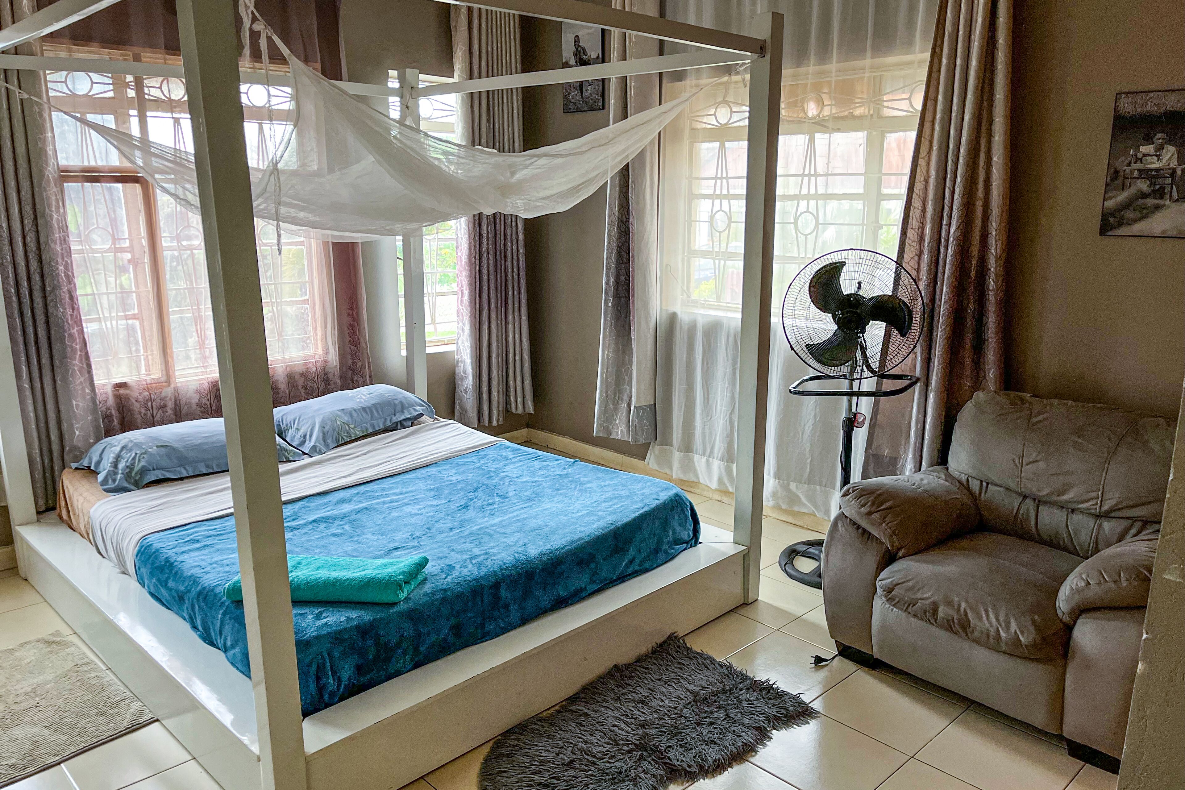 A bedroom with a canopy bed, a sofa, and a standing fan.