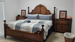 Una camera da letto con un letto a baldacchino in legno, un comodino, un cesto di vimini e un quadro appeso al muro.