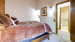 Un dormitorio con cama, cabecera de madera, un cuadro enmarcado y una puerta que da al baño.