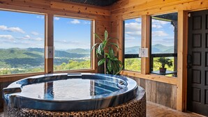 Une cabane en bois dotée d’un bain à remous, de grandes fenêtres et offrant une vue sur les montagnes.
