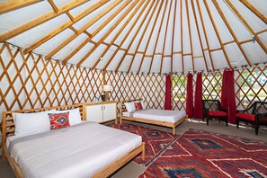 A yurt with two beds, a small table, and a red curtain.