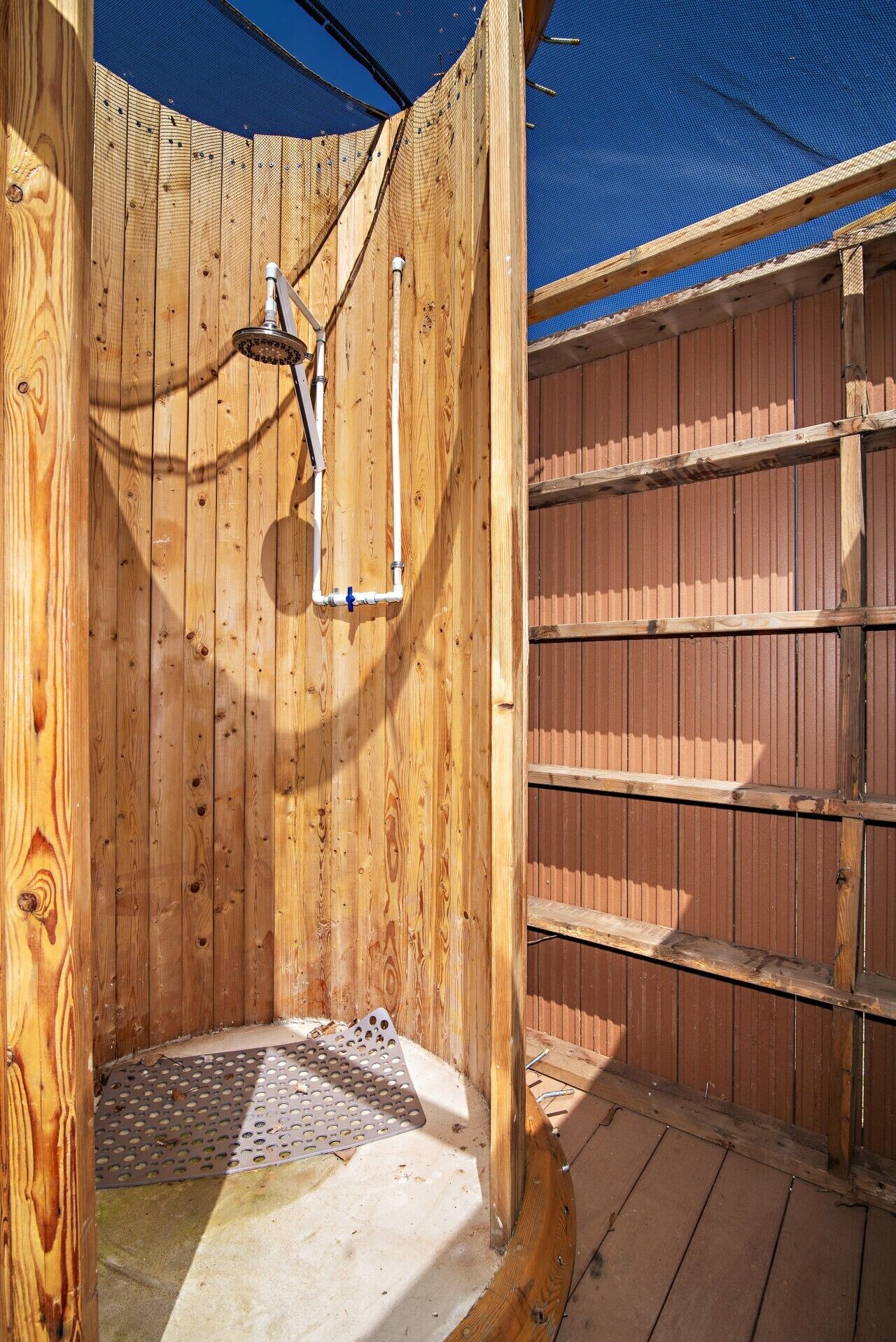 A wooden outdoor shower with a metal showerhead and a blue tarp overhead.