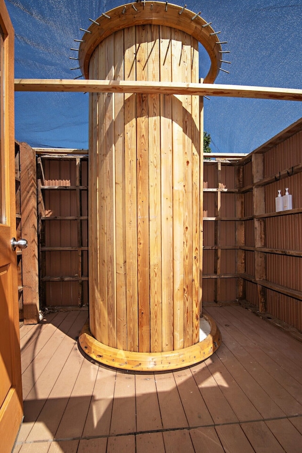 A wooden cylindrical structure with a door, surrounded by wooden walls and a wooden deck.