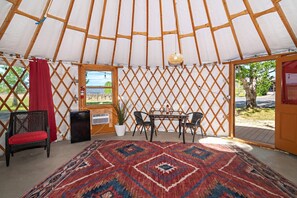 A yurt with a table and chairs, a red curtain, and a patterned rug.