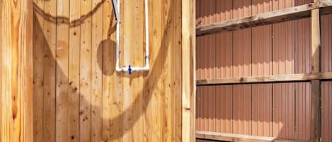 A wooden outdoor shower with a metal showerhead and a blue tarp overhead.
