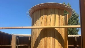 Una estructura de madera con una parte superior circular y listones verticales, posiblemente un mueble o elemento de utilidad.