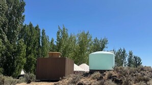 Two large cylindrical structures, possibly storage tanks, in a dry, bushy area with tall trees in the background. - Yurt #7 - Glamping by the Gorge & Cave B (Quincy)