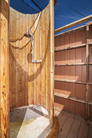 A wooden outdoor shower with a metal showerhead and a blue tarp overhead.