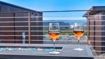 Deux verres à vin portant l’inscription « Cave B Estate Winery » sont posés sur une table, avec en arrière-plan une vue sur un bâtiment et un paysage.