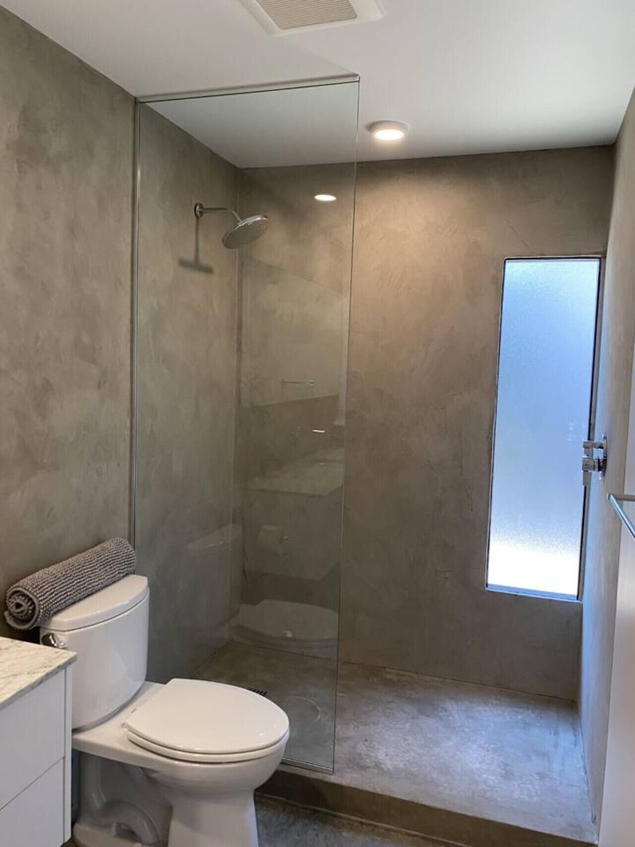 A modern bathroom with a glass-enclosed shower, a toilet, and a window providing natural light.