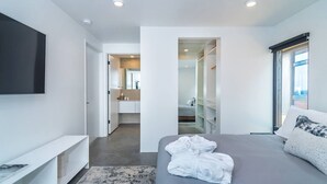 Habitació d'hotel moderna amb un llit gran, televisió de pantalla plana penjada a la paret, un vestidor i un bany amb mirall i rentapel.