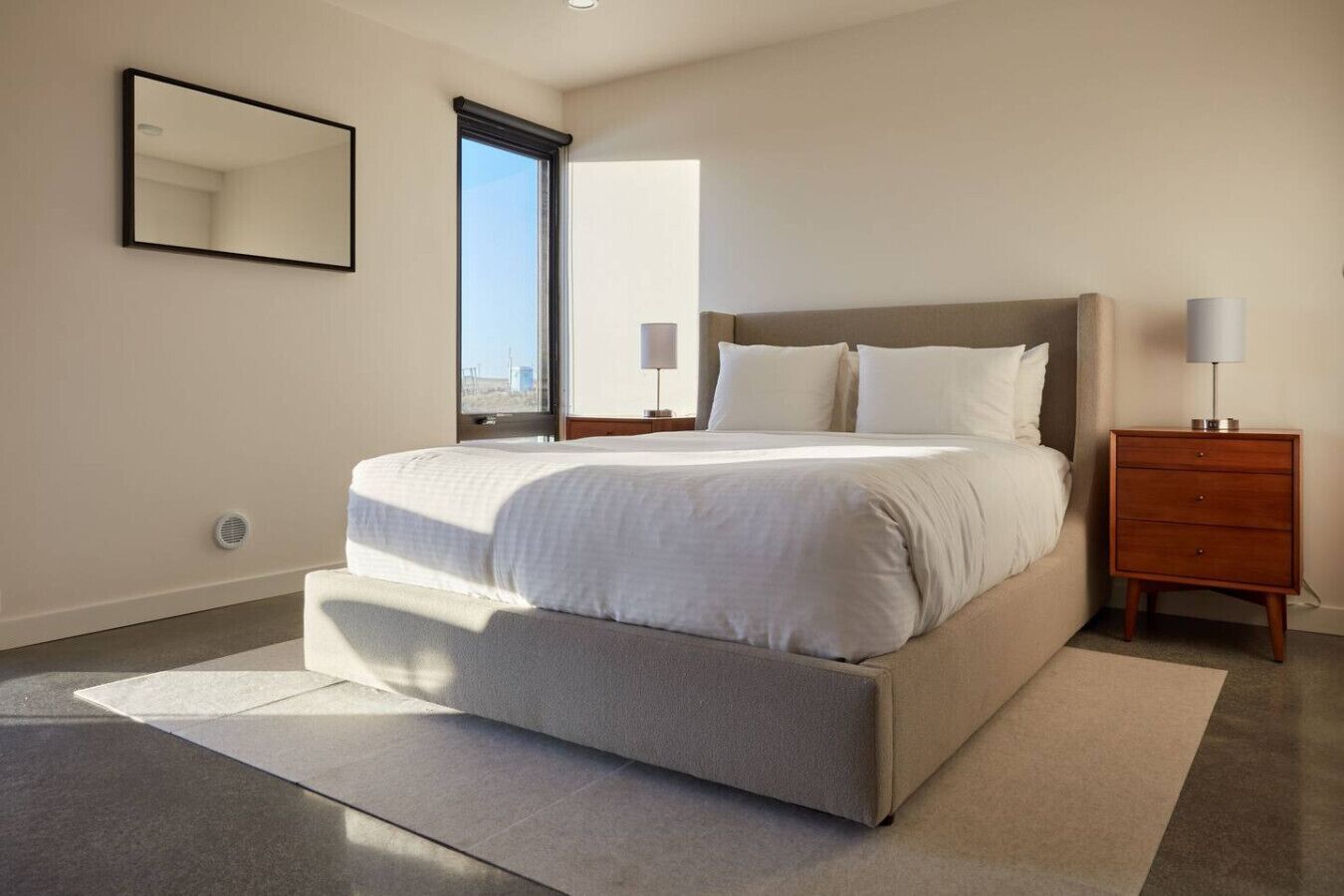 Ein modernes Schlafzimmer mit einem großen Bett, einem Nachttisch, einem Spiegel und einem Fenster.