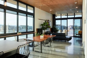 A modern office space with large windows, a wooden ceiling, and a dining area with a table and chairs.