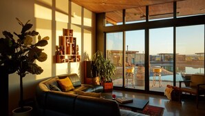 A modern living room with a large window, a sofa, a coffee table, and a bookshelf. - The Point at the Lakes - Cave B (Quincy)