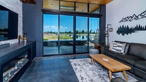 A modern living room with a large sliding glass door leading to a scenic outdoor view, a dark leather sofa, a wooden coffee table, and a TV on a built-in shelf. - Rustic Elegance at the Gorge (Quincy)