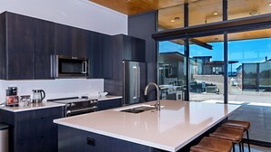 A modern kitchen with dark cabinetry, stainless steel appliances, and a large island with bar stools. - Rustic Elegance at the Gorge (Quincy)