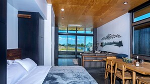 A modern hotel room with a large bed, a dining area with wooden furniture, and a scenic view through large windows. - Rustic Elegance at the Gorge (Quincy)