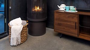 Ein modernes Wohnzimmer mit Kaminofen, Fernseher und Korbstuhl.