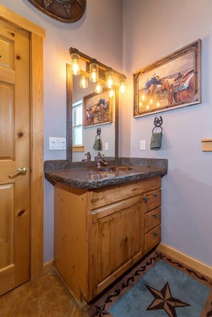 Een badkamer met houten kastjes, een wastafel, een spiegel met verlichting en een schilderij aan de muur.