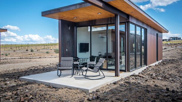 A modern, glass-enclosed building with a patio area featuring outdoor furniture.