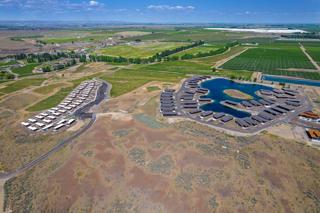 Eine Vogelperspektive auf einen großen Industrieanlagenkomplex mit mehreren Lagerhallen, einem kreisförmigen Wasserspiel und umliegenden Grünflächen.