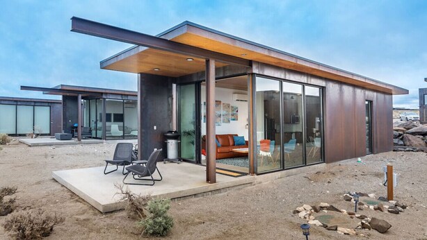 Une maison moderne dotée d’un patio entièrement vitré, d’un coin repas et d’un salon avec un canapé et des fauteuils.